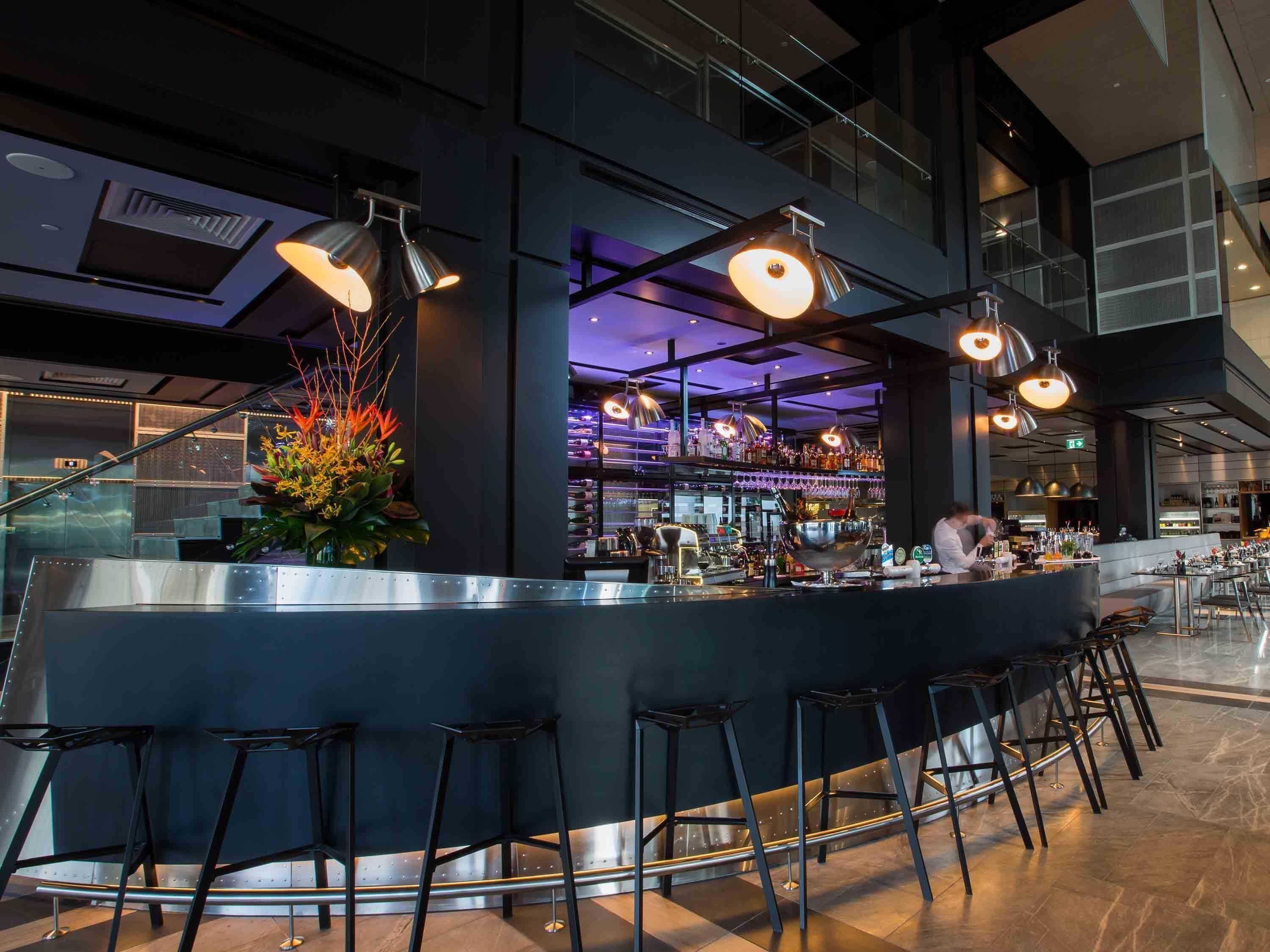 A modern bar area with a curved counter, multiple stools, and overhead lighting.