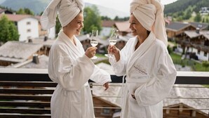 Two individuals in white robes toasting with wine glasses on a balcony with a mountainous backdrop. - Panoramahotel Oberjoch (OBERJOCH)