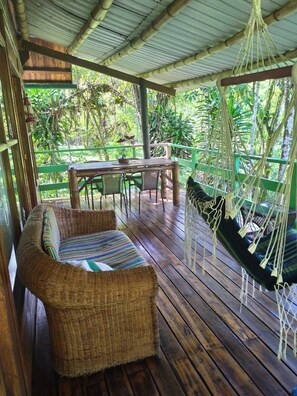 A wooden deck with wicker furniture, a hanging hammock, and a table with chairs. - Mindo Eco chalet (Mindo)