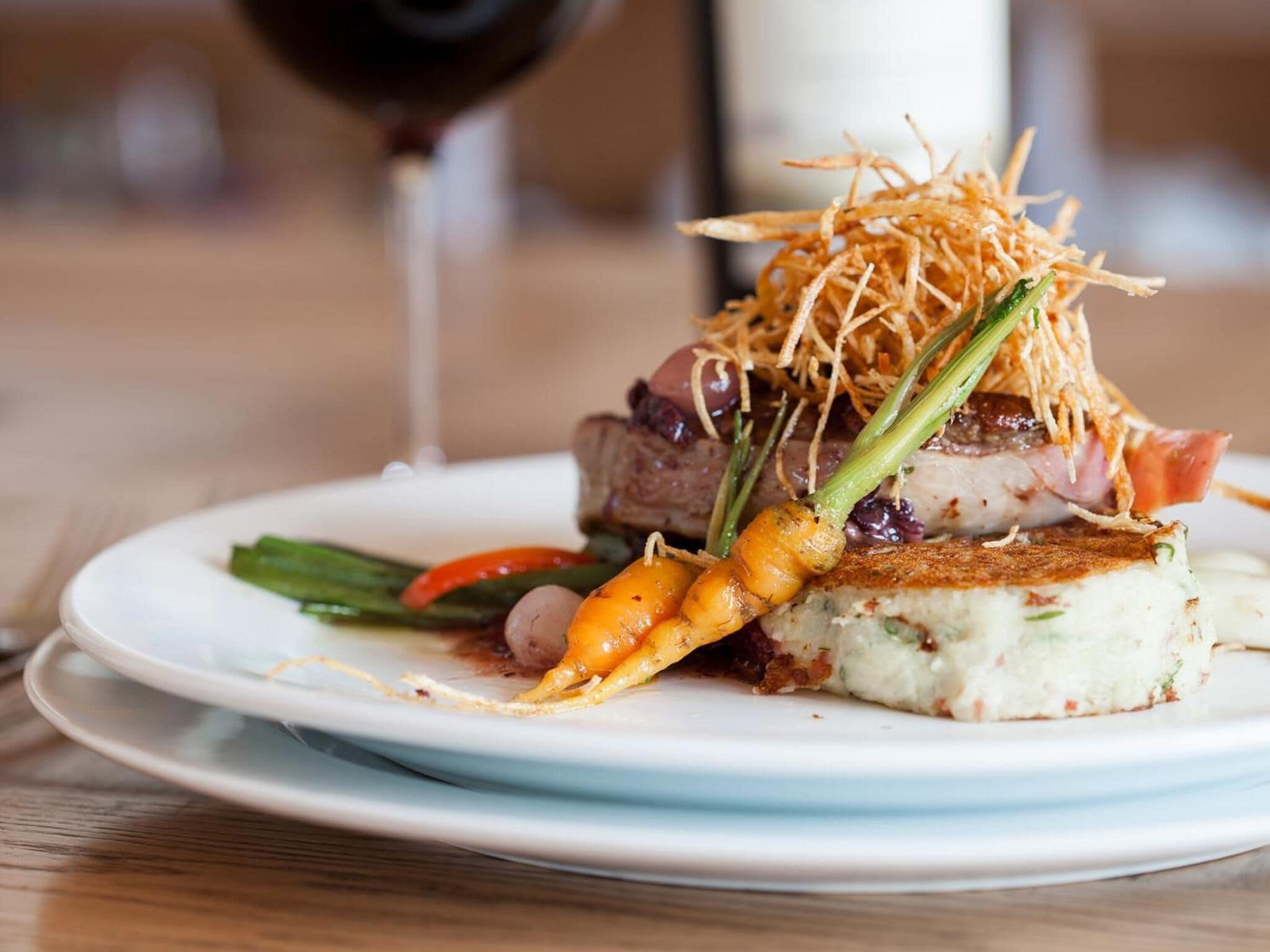 A plate of food with a piece of meat, vegetables, and a garnish on top.