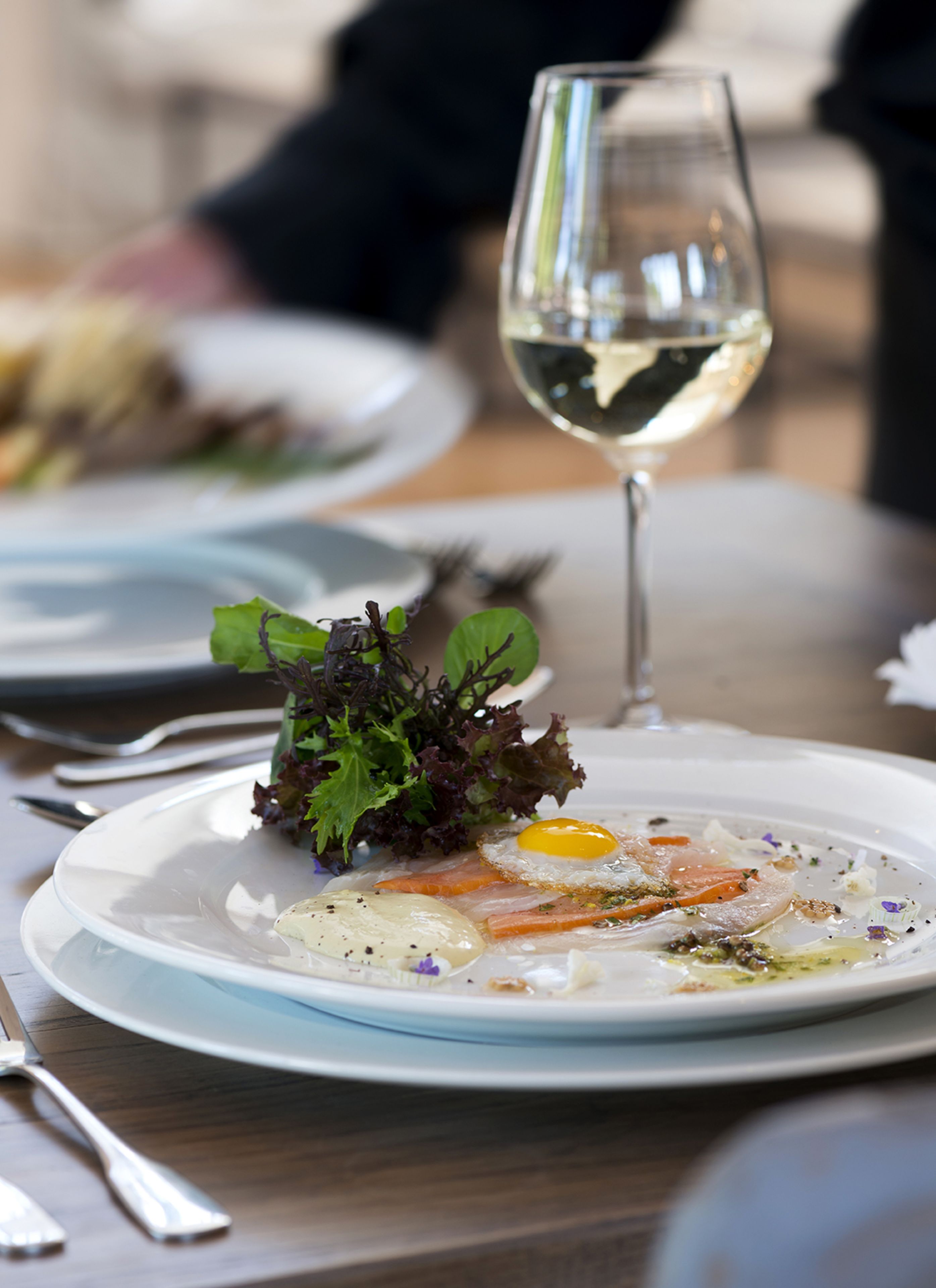 Uma mesa de jantar com pratos de comida, um copo de vinho branco e talheres.