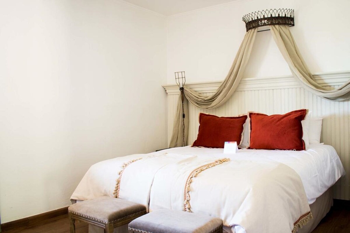 A neatly made bed with a canopy, a small bench, and a radiator on the wall.