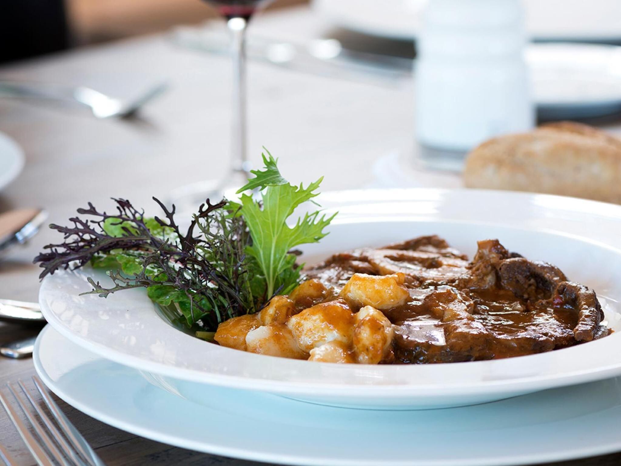 Un plato de comida con una copa de vino y un vaso de agua sobre una mesa.