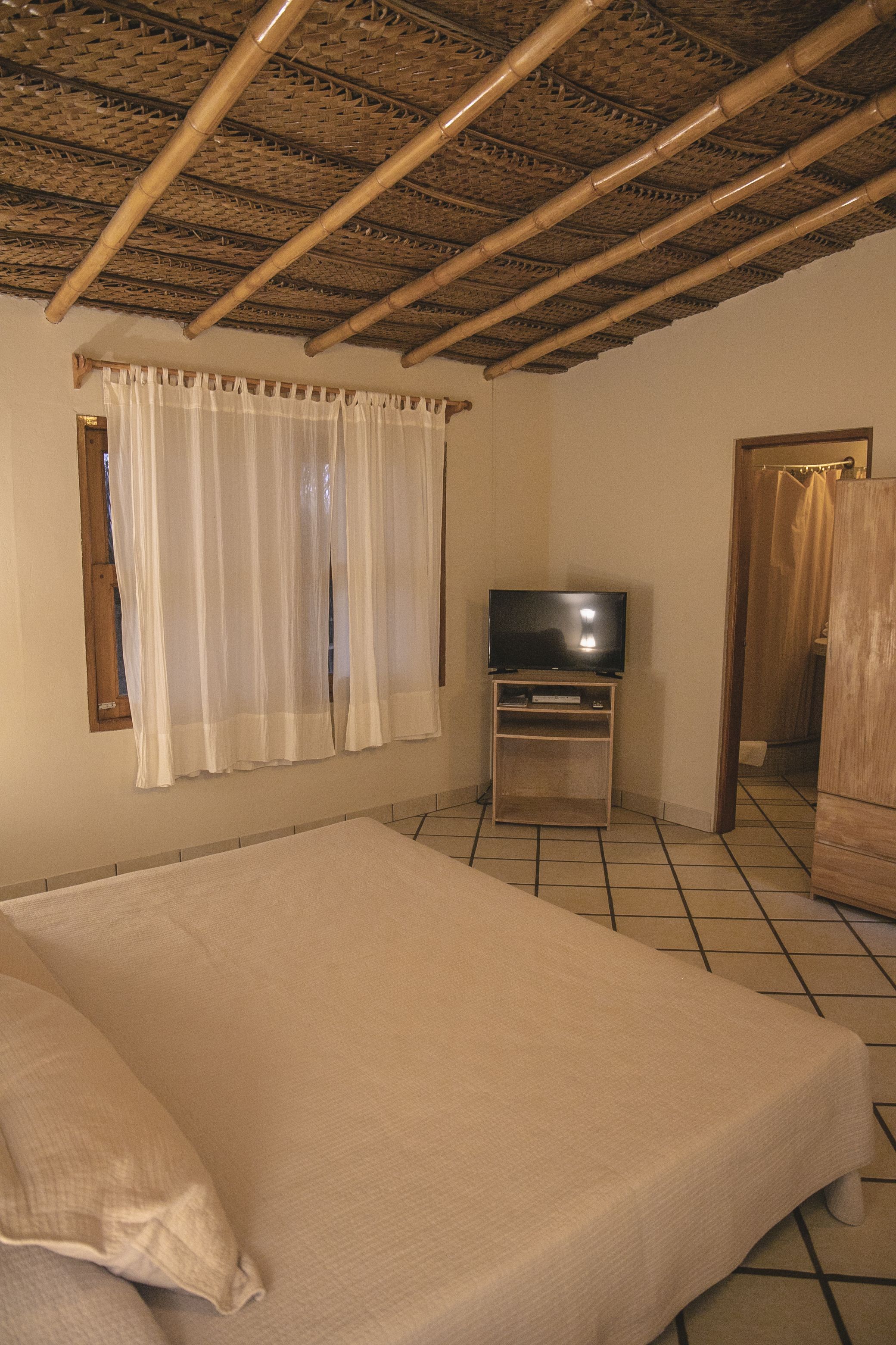 Une chambre à coucher avec un lit, des rideaux, une télévision et une armoire en bois.