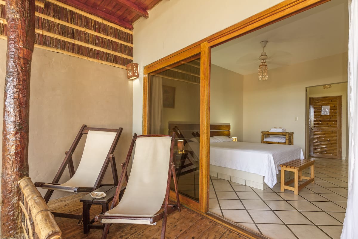 A room with a bed, a wooden bench, and a chair with a white cushion.