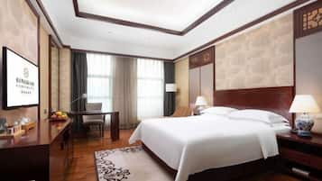 A hotel room with a large bed, a desk, a chair, and a TV on the wall.