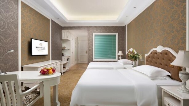 Une chambre d’hôtel équipée d’un lit, d’un bureau, d’une chaise, d’une télévision et d’une fenêtre avec des stores.