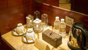 Un mini-bar dans une chambre d’hôtel, avec des tasses à thé, des bouteilles et une bouilloire.