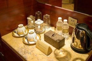 Un mini-bar dans une chambre d’hôtel, avec des tasses à thé, des bouteilles et une bouilloire.