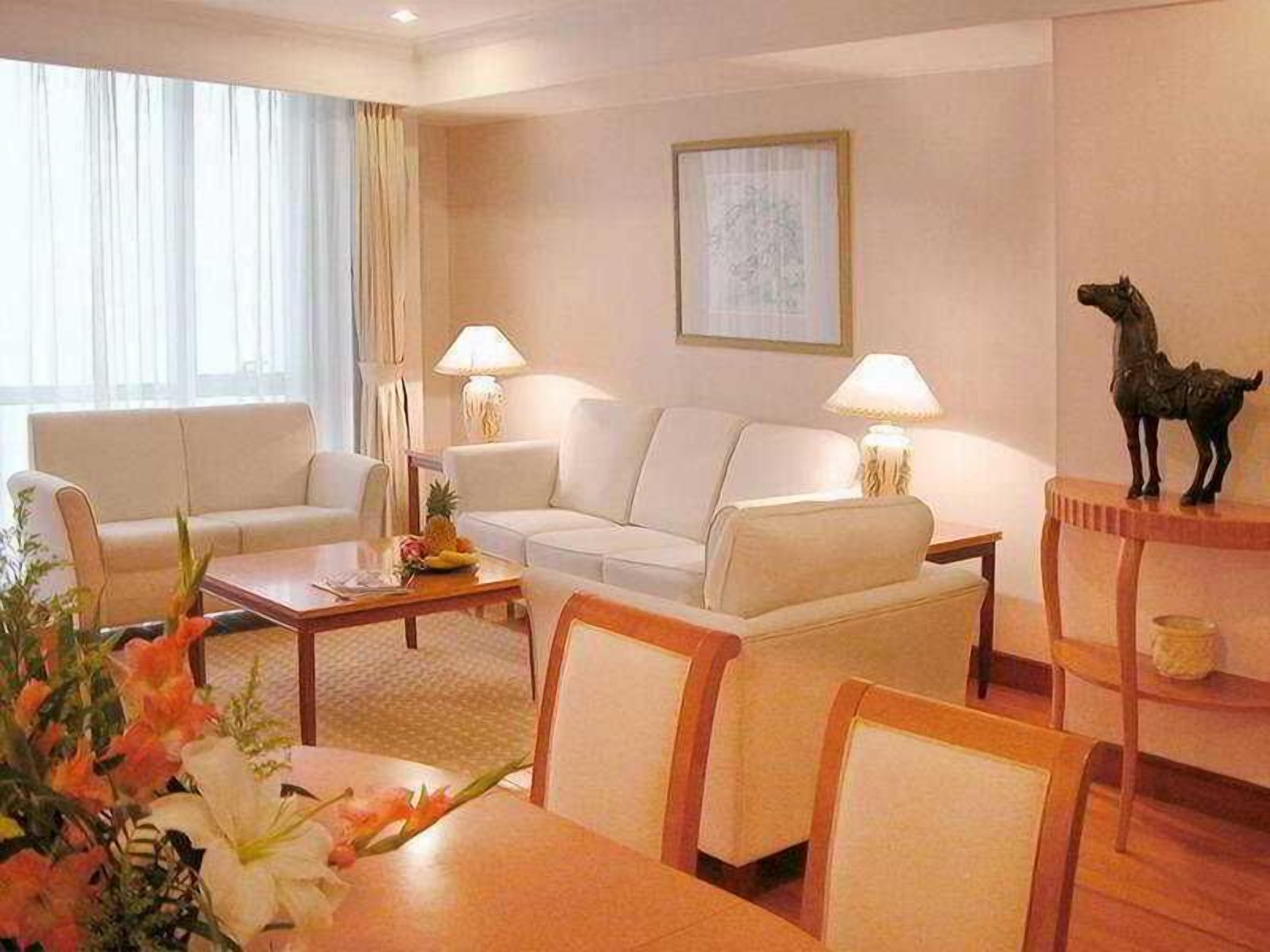 Habitación de hotel con sofá, una mesita de centro, una mesa de comedor con sillas, una lámpara y un cuadro en la pared.