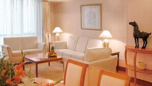 Ein Hotelzimmer mit einer Sofagarnitur, einem Couchtisch, einem Esstisch mit Stühlen, einer Lampe und einem gerahmten Bild an der Wand.