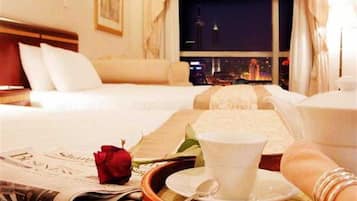 Habitación de hotel con una cama, un cesto con una taza y platillo, una rosa y un periódico.