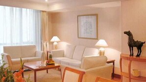 Een hotelkamer met een zithoek, een salontafel, een eettafel met stoelen, een lamp en een lijst met een afbeelding aan de muur.
