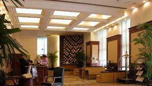 Een hotellobby met een receptiebalie, een zithoek en een behang met patroon.