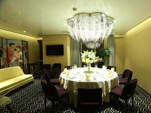 Une salle à manger avec une table ronde, des chaises, un lustre, un canapé et un téléviseur fixé au mur.