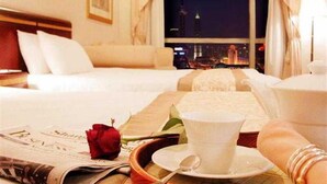 Ein Hotelzimmer mit Bett, Tablett mit Tasse und Untertasse, einer Rose und einer Zeitung.