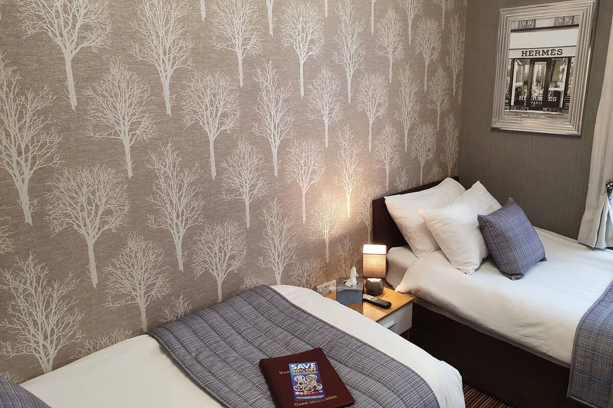 A hotel room with two beds, a nightstand with a lamp, a framed picture on the wall, and a book on the bed.