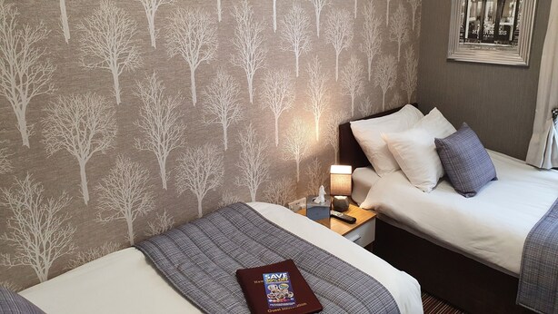 Ein Hotelzimmer mit zwei Betten, einem Nachttisch mit Lampe, einem gerahmten Bild an der Wand und einem Buch auf dem Bett.