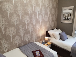 A hotel room with two beds, a nightstand with a lamp, a framed picture on the wall, and a book on the bed.