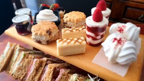 Eine Auswahl an Desserts, darunter Scones, Sandwiches und Crème Puffs, auf einer Holzbrett.