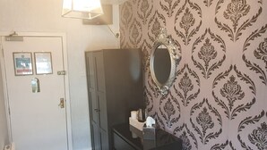 Ein Zimmer mit einer weißen Tür, einem schwarzen Kleiderschrank, einem Spiegel und Tapete mit Muster.
