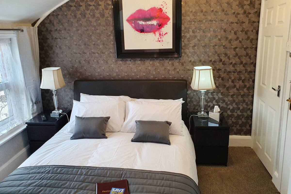 A neatly made bed with white linens and two pillows, a framed artwork above it, and two bedside tables with lamps.