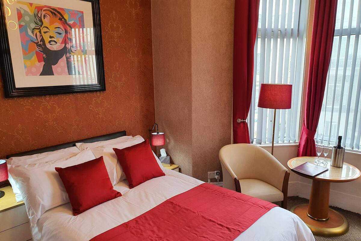 A hotel room with a bed, a chair, a table, a lamp, and a window with curtains.