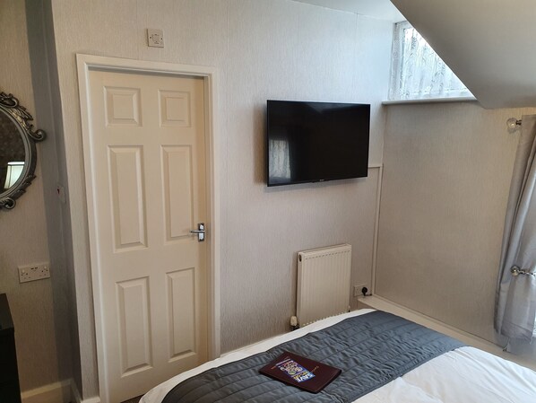 A bedroom with a bed, a television mounted on the wall, a door, and a radiator.