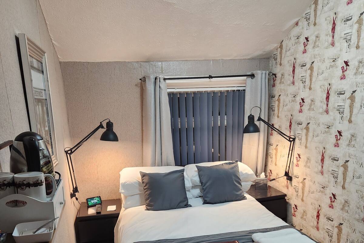 A neatly arranged hotel room with a bed, bedside lamps, a nightstand, a coffee maker, and a wall clock.