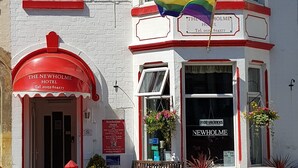 Das Newholme Hotel mit rotem Markisenvorzelt, einer Regenbogenflagge und einem Schild mit der Aufschrift 'Keine freien Zimmer'.