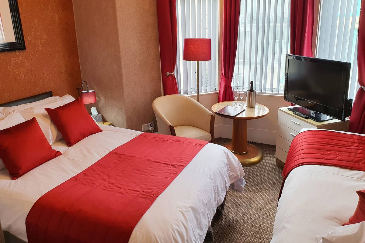 A hotel room with a bed, a chair, a small table, a TV, and a window with curtains.