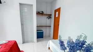 Une pièce comprenant un lit, une table rouge, une glacière bleue et une porte donnant sur une salle de bain.
