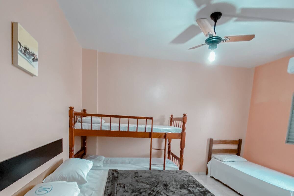 Une chambre avec un lit superposé, un lit simple, un ventilateur de plafond et une petite table de chevet.