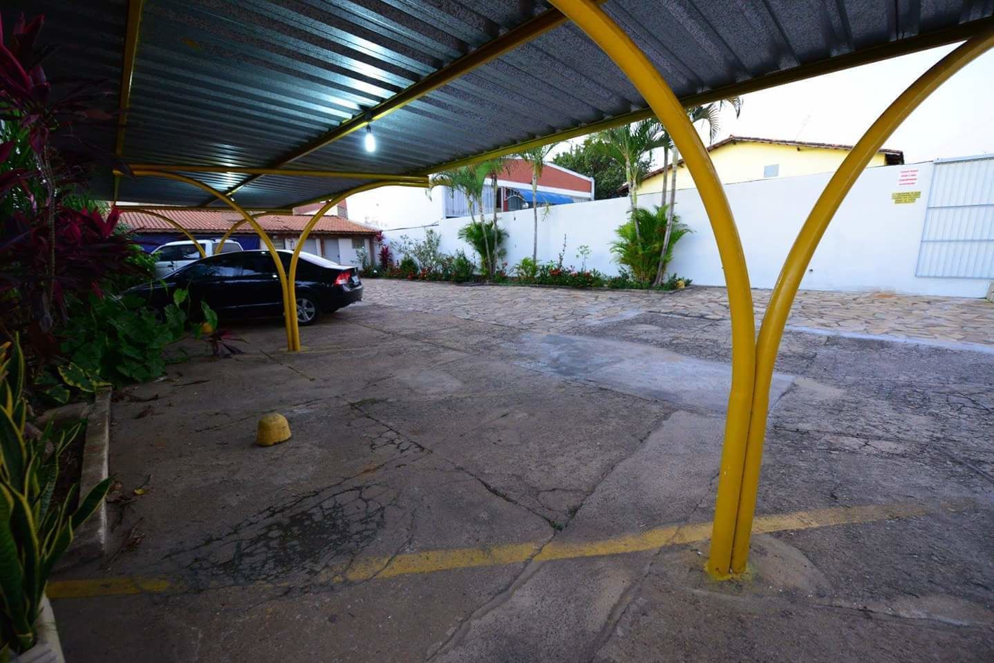 Un espace de stationnement couvert, doté d’un sol en béton, de piliers de soutien jaunes et d’une voiture garée à l’abri.