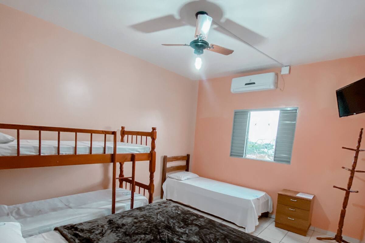 Une chambre avec des lits superposés, un bureau, une chaise, une armoire et un ventilateur de plafond.