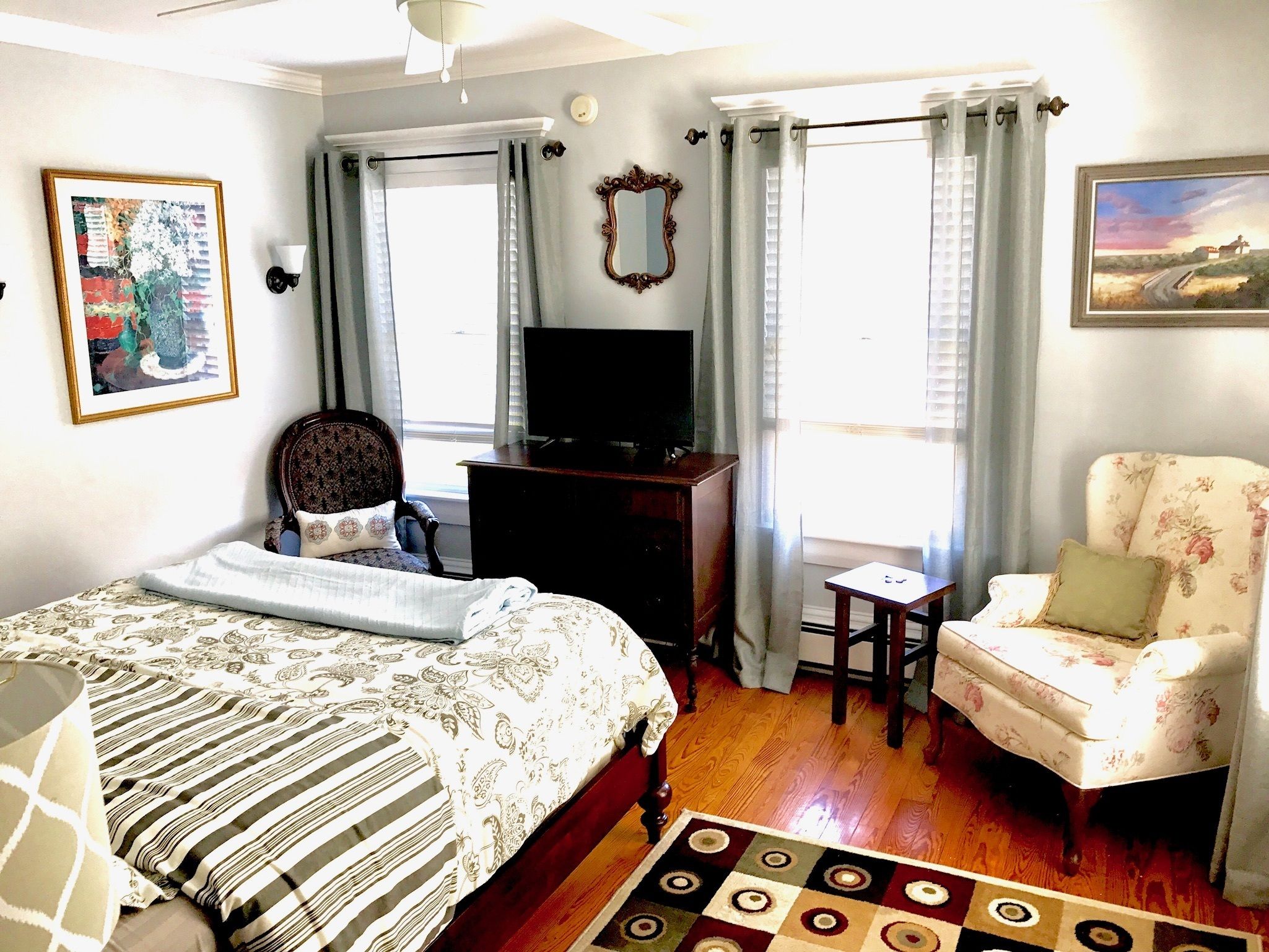 A bedroom with a bed, a chair, a dresser, a television, and a window with curtains.