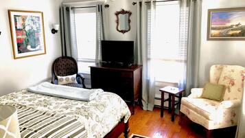 A bedroom with a bed, a chair, a dresser, a television, and a window with curtains.