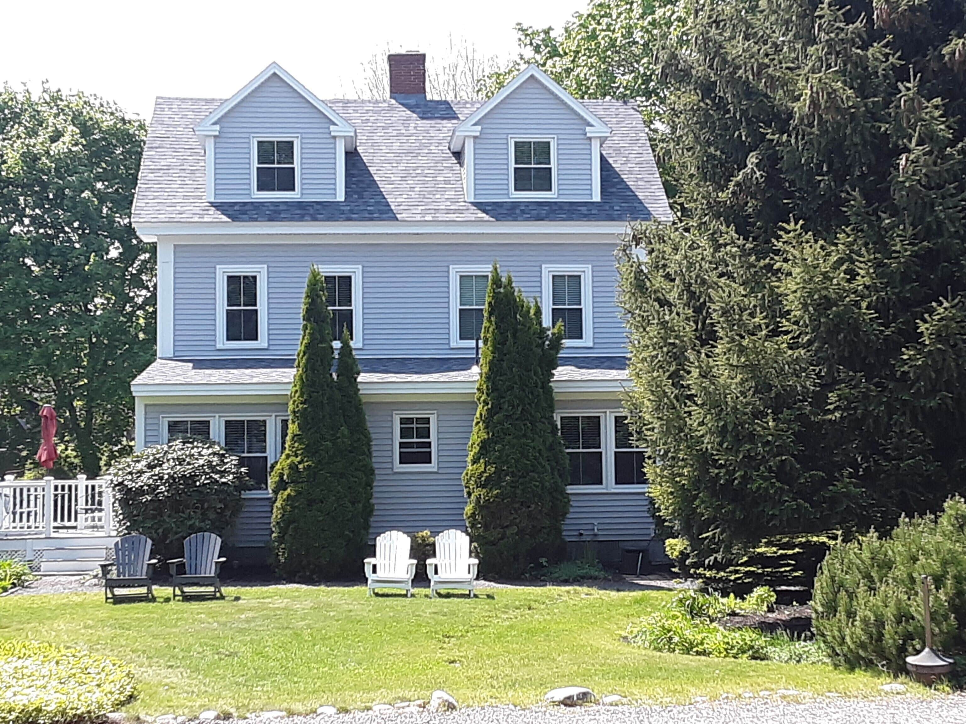 A two-story house with a front porch, two large windows on the second floor, and two tall evergreen trees in the front yard.