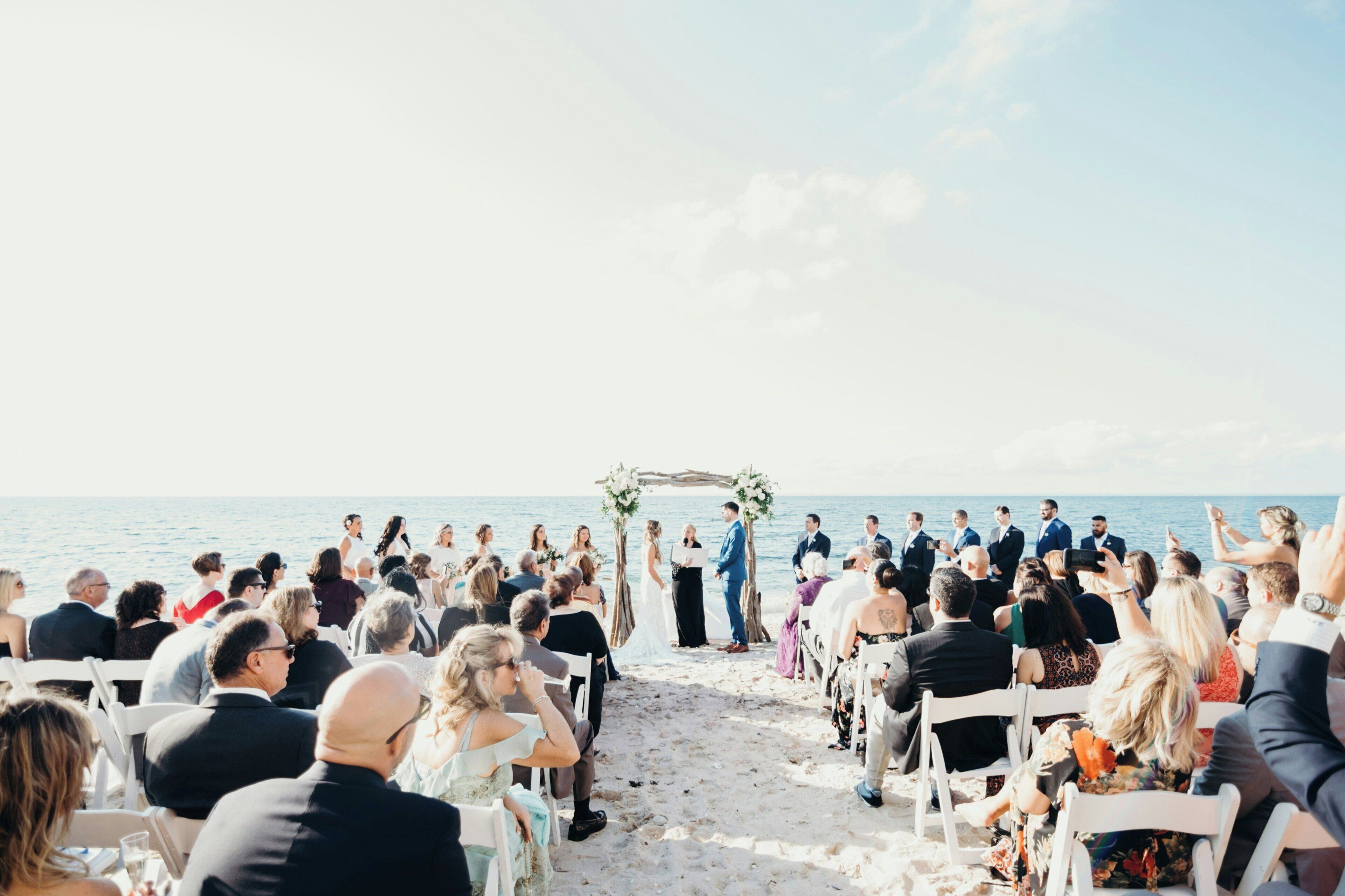 Une cérémonie de mariage sur la plage, les invités étant assis sur des chaises blanches, face à l’allée.