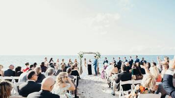 Une cérémonie de mariage sur la plage, les invités étant assis sur des chaises blanches, face à l’allée.