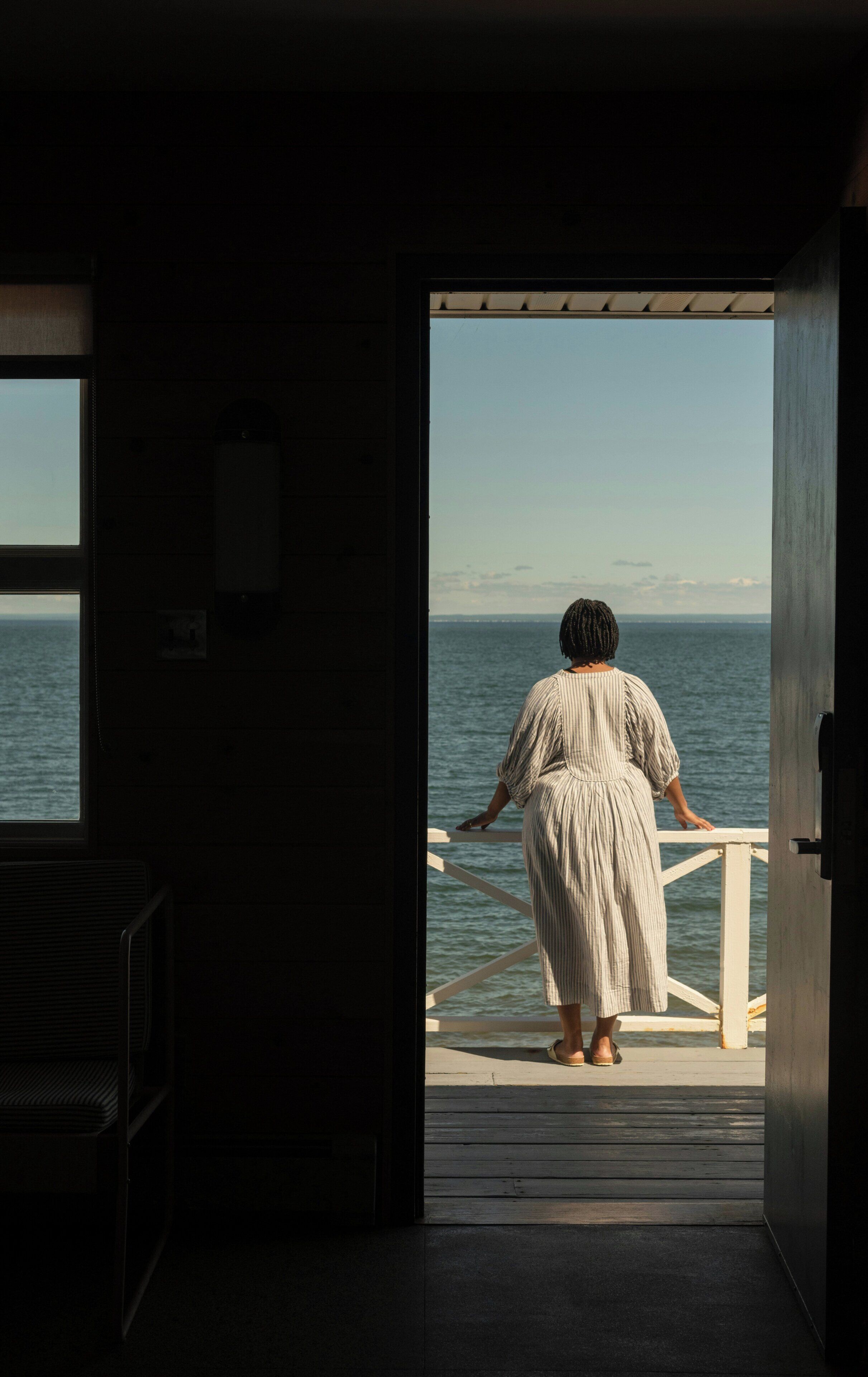 A room with a large window and a door leading to a balcony overlooking the sea.