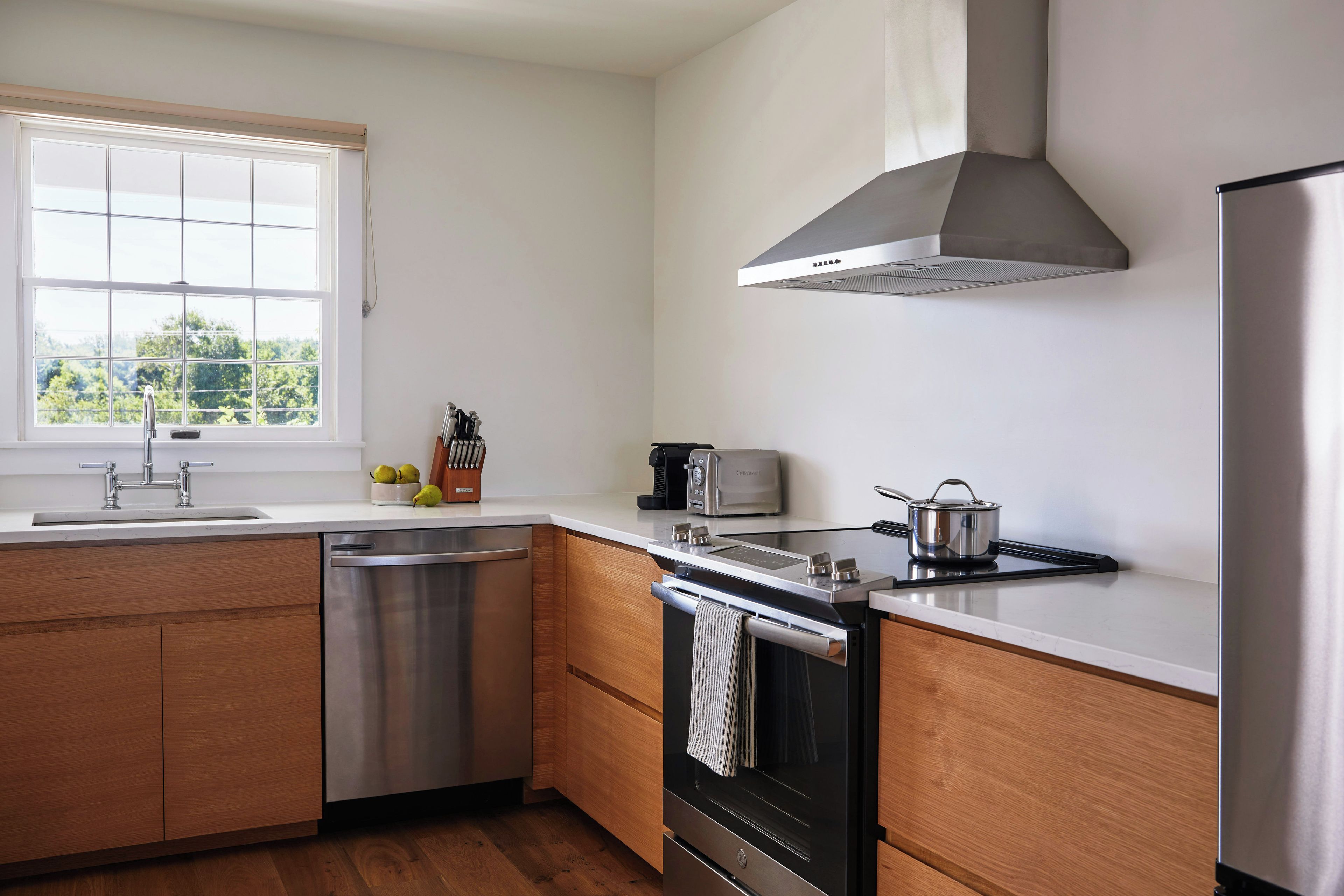 A modern kitchen with a dishwasher, stove, toaster, and a window with a view of greenery.