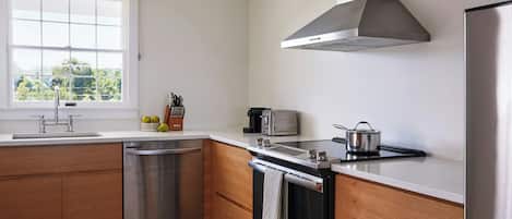 A modern kitchen with a dishwasher, stove, toaster, and a window with a view of greenery.