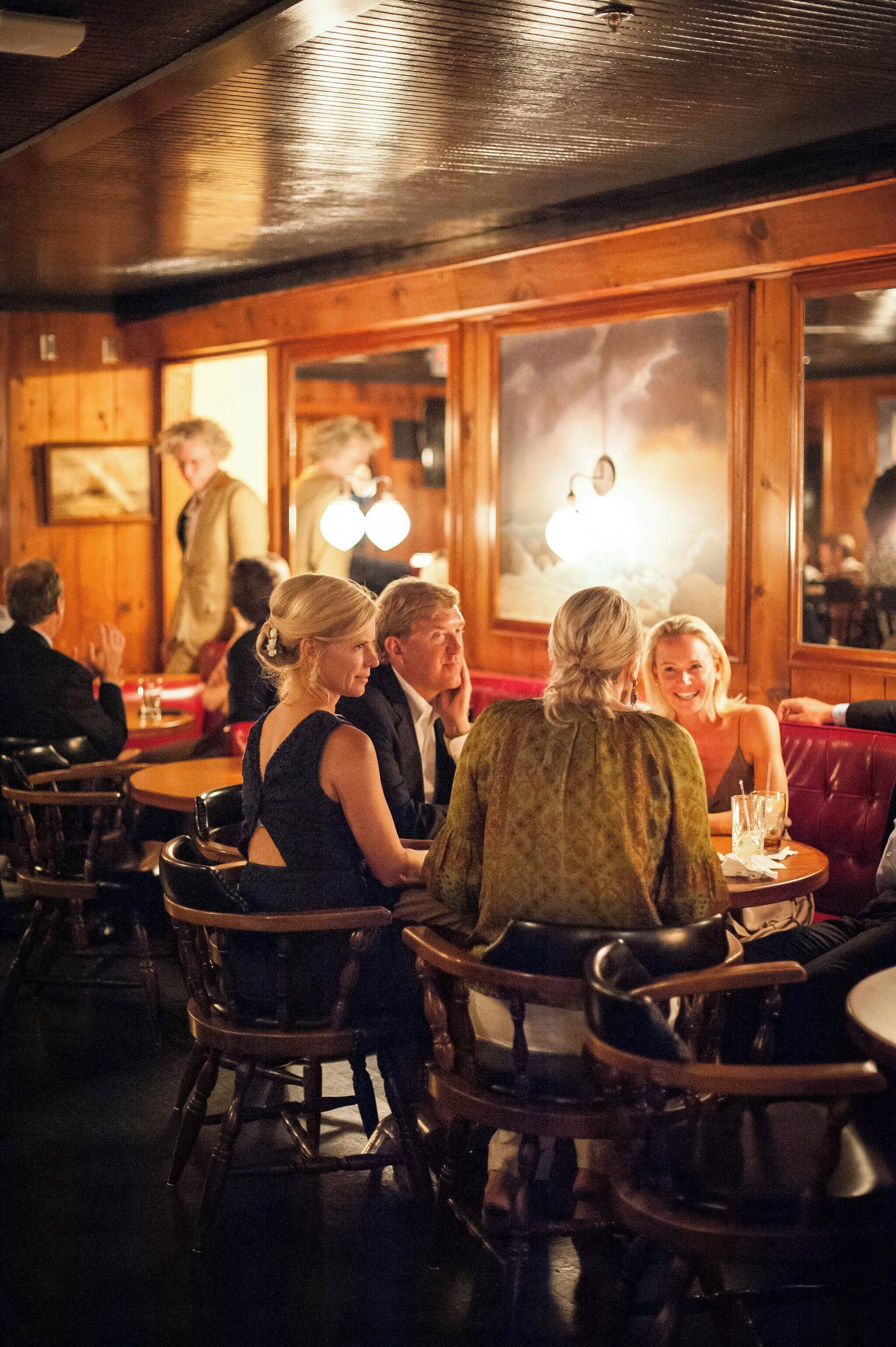 A restaurant interior with wooden walls, round tables, and leather booths.