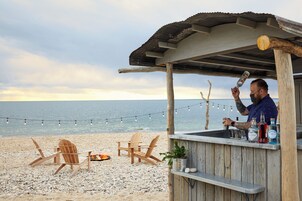 Un bar de playa con sillas de madera y una pequeña mesa, con vista al mar.
