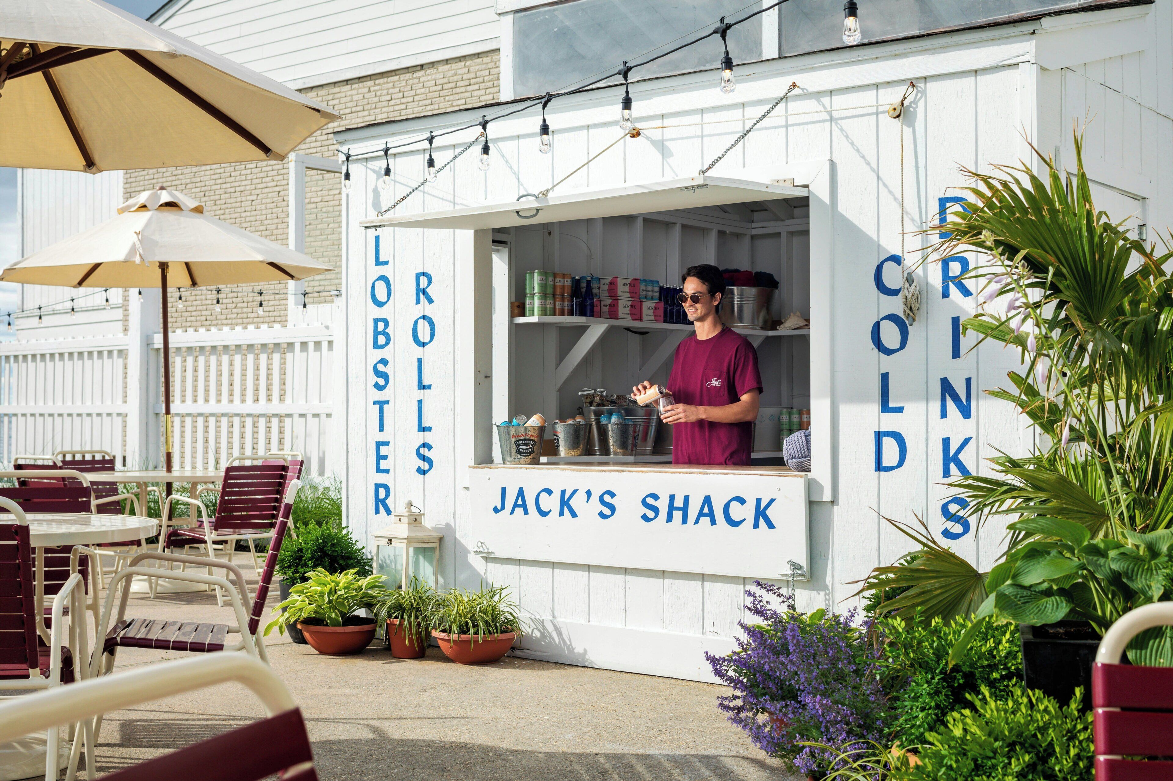 A white outdoor seating area with tables and chairs, a sign for 'Jack's Shack,' and potted plants.