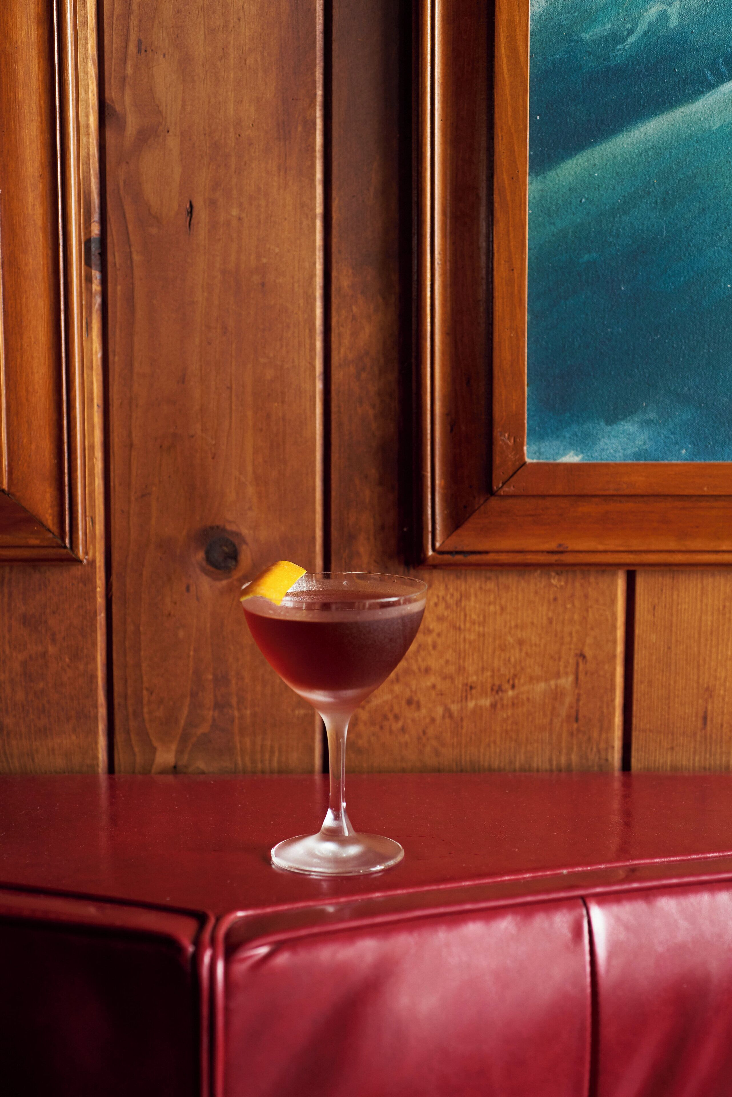 A wooden panel wall with a framed artwork and a glass table with a red leather bench.