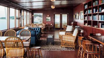A cozy, well-lit room with wooden floors, a large bookshelf, and comfortable seating areas.
