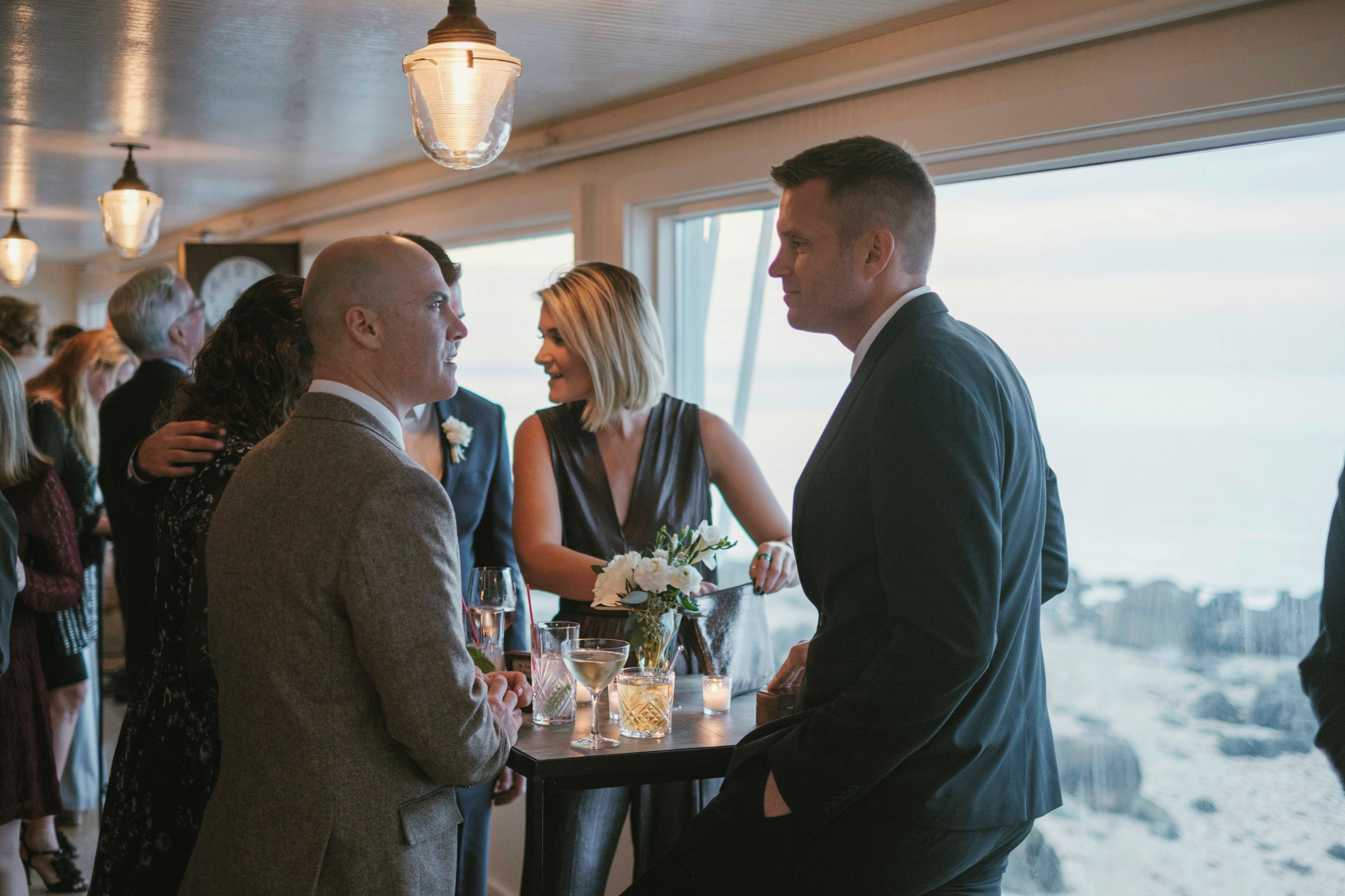 A group of people at a social event inside a building with a view of the outdoors.