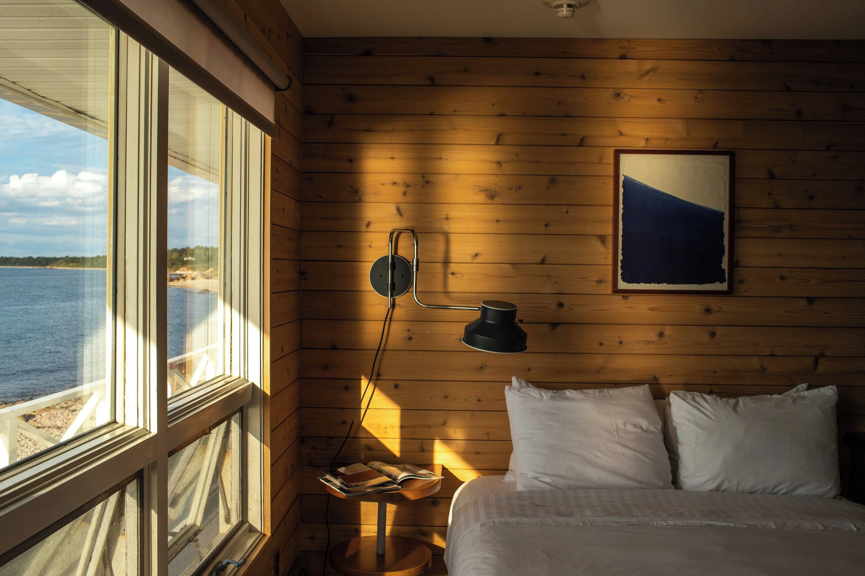 A room with a bed, a table with books, a lamp, and a painting on the wall.